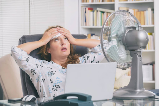 Woman sitting back in her office chair sweating due to broken AC
