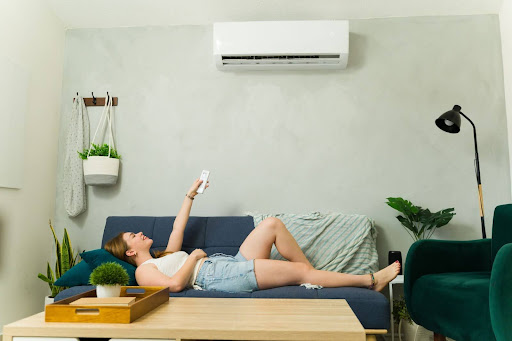 Homeowner chilling on the couch, using a remote to turn on a mini split AC unit.